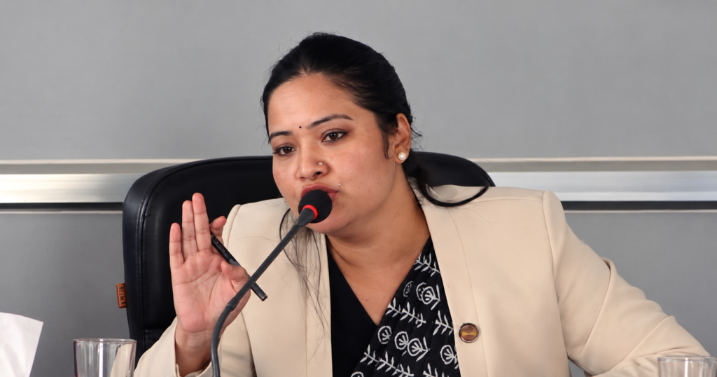 मन्त्री प्रतिभा रावल हातमा कलम समातेर माइक्रोफोनमा बोल्दै गरेको तस्बिर।