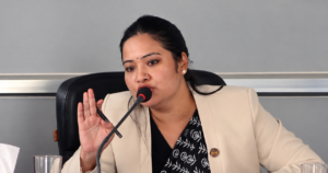 मन्त्री प्रतिभा रावल हातमा कलम समातेर माइक्रोफोनमा बोल्दै गरेको तस्बिर।
